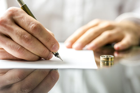 close-up of man's hand signing divorce document with wedding ring on table